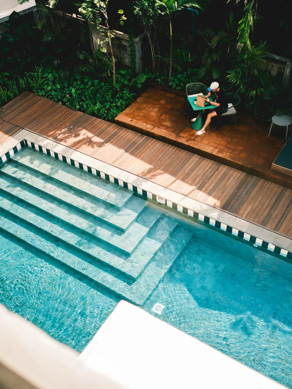 The shared pool seen from above, with tiled steps, a wooden deck, daybeds and palms