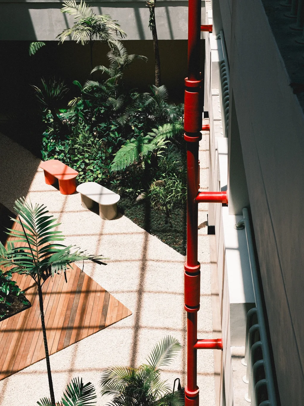 The atrium seen from above: a red column, a wooden deck, palms and plants, with a bench and low seats