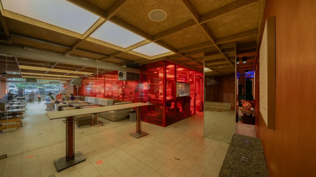 A long high table and a red glass box inside The Square Room, with the outside visible beyond the glass
