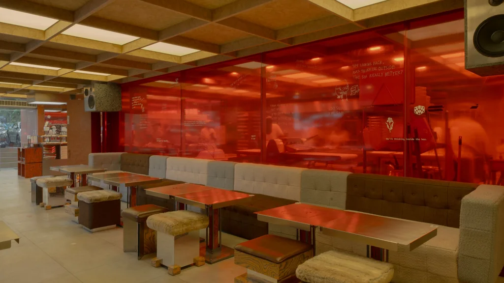 Upholstered booth seating and tables in front of red tinted glass at The Square Room