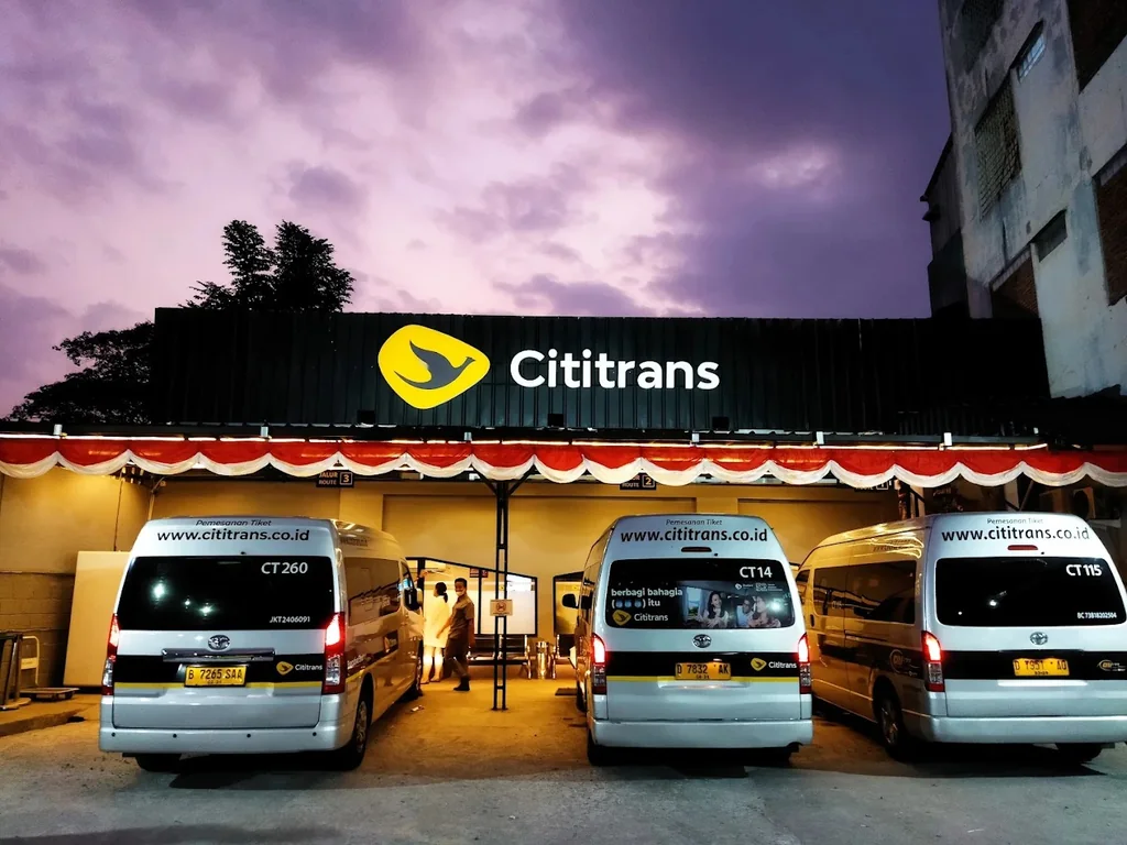 Cititrans Pasteur at dusk: three white shuttle vans parked in front of the lit Cititrans sign